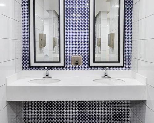 Restroom vanity with dual sinks and mirrors. White, blue and dark gray tile surfaces.